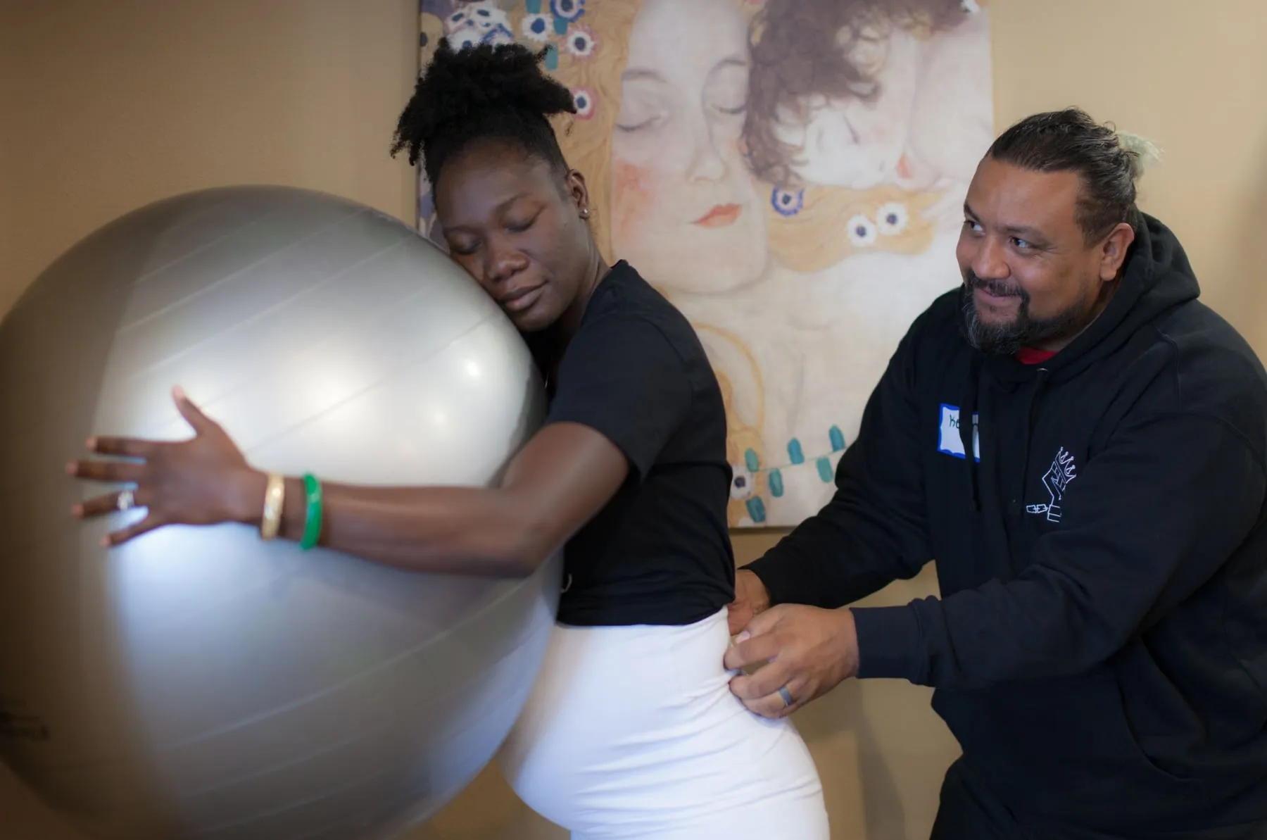 A pregnant woman leaning on a birth ball while her partner supports her during a class