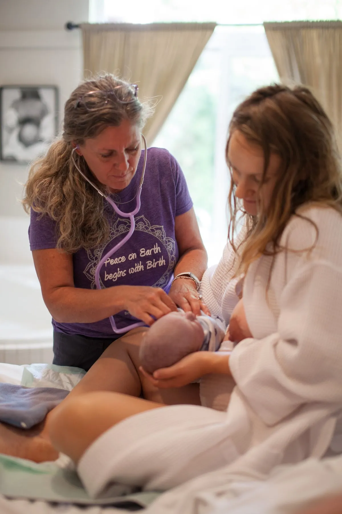 A midwife listening to a newborn with a stethoscope while the mother holds her baby