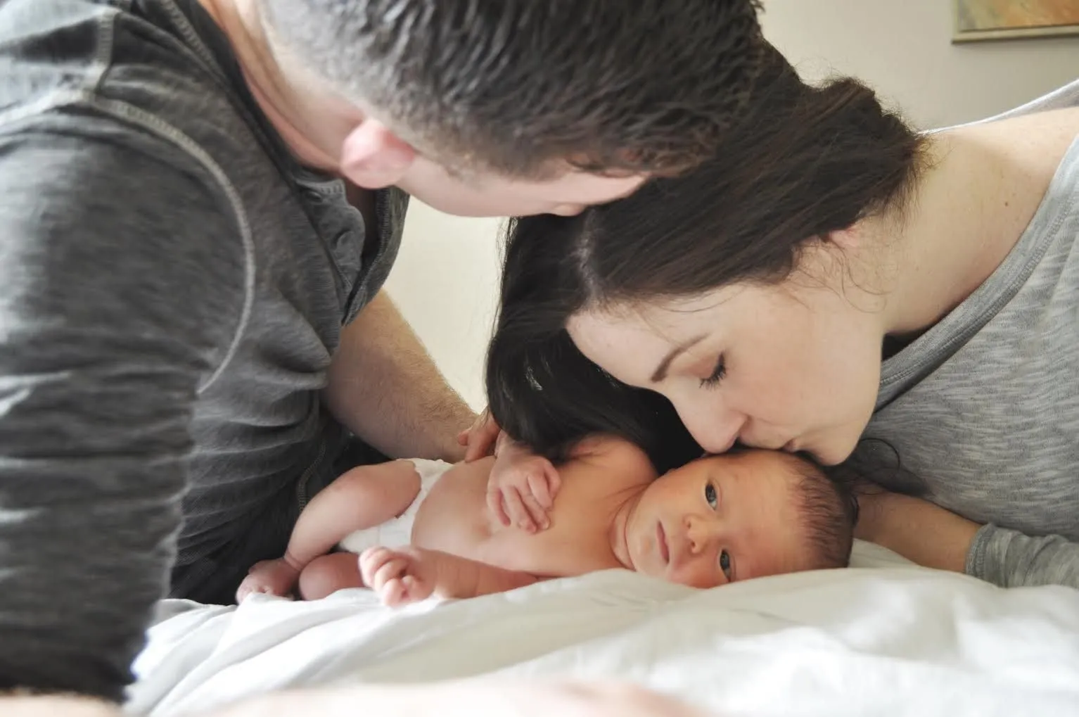 Parents kissing their newborn baby on a bed after the birth